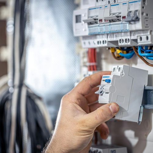 A male electrician works in a switchboard with an electrical connecting cable.